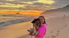 Lorea segurando cachorro em praia e sorrindo