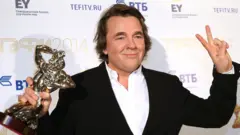 Мужчина в костюме держит в руках скульптуру