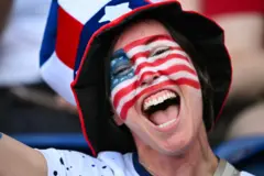 Mulher sorri com a bandeira americana desenhada no rosto, usando um chapéu com as cores dos Estados Unidos