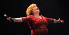 Susan Boyle, com vestido vermelho e braços estirados, canta durante o musical 'I Dreamed A Dream' no Teatro Real de Newcastle, no Reino Unido, em 2012