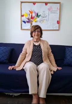 Retrato de corpo inteiro de Celi Ferreira, mulher de 82 anos, sentada no sofá