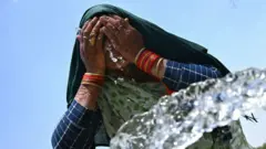 A woman washes her face with water to cool off during a hot summer day near the India Gate in New Delhi