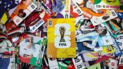 Álbum da Copa do Mundo ao meio com várias figurinhas de jogadores ao redor