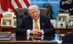 الرئيس الأمريكي دونالد ترامب جالسا على المكتب البيضاوي بالبيت الأبيض ومرتديا بذلة ووقميصا أبيض وربطة عنق صفراء.