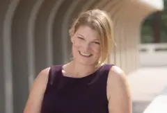 Candice Odgers é uma mulher branca e loira. Ela está sorrindo para a foto e usando uma blusa roxa.