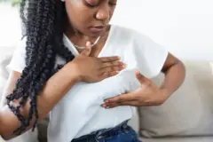 Jeune femme afro-américaine palpant son sein par elle-même qu’elle s’inquiète du cancer du sein.