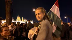 Una joven con el pelo largo trenzado sostiene una bandera de Hungría durante las celebraciones frente al parlamento nacional, a orillas del río Danubio.