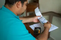 Homem diante da mesa com papéis, boletos e calculadora