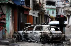 Un auto calcinado y atravesado en medio de una calle.