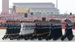 Soldados em uniformes cerimoniais marcham em frente a um pódio lotado