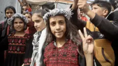 Niños palestinos reunidos en una celebración tras el anuncio de cese al fuego. Una de ellos, en el medio del plano, posa ante la cámara haciendo con sus dedos el símbolo de la paz.