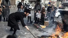 رجل يهودي متشدد يحرق بقايا الطعام ضمن طقوس "سريفات حاميتس" عشية عيد الفصح اليهودي الذي يبدأ عند غروب الشمس، في القدس، 11 أبريل/نيسان 2025. 