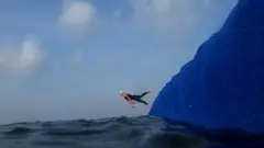 Nadador pula de uma plataforma para mergulhar no mar