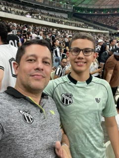 Pai e filho posam para foto. Eles estão em um estádio de futebol e usam camisas do time do Ceará.