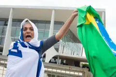 Manifestante enrolada na bandeirarodada gratis cassinoIsrael segura uma bandeira do Brasilrodada gratis cassinofrente ao prédio do STF