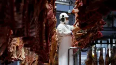 Frigorífico brasileiro, homem trabalha rodeado de pedaços de carne bovina