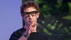 Mark Zuckerberg wearing thick black rimmed smart glasses and gesturing with his hand.