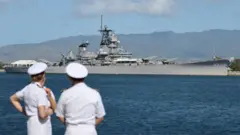 Três marinheiros conversam com um navio de guerra dos EUA ao fundo no Havaí.