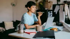 Devojka priča na telefon, ispred njen je laptop