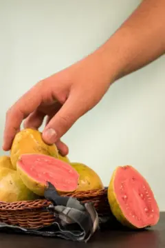 Mão pega uma goiaba de um cesto das frutas sobre uma mesa