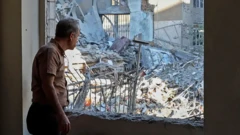 مردی از درون اتاقی که پنجره‌اش ویران شده به ویرانه‌های بیرون نگاه می‌کند