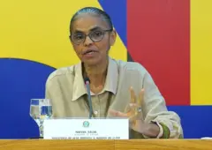 Foto de Marina Silva durante entrevista coletiva com fundo azul, amarelo e vermelho