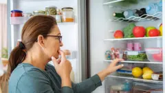 Mulher olhando interior da geladeira cheia de alimentos