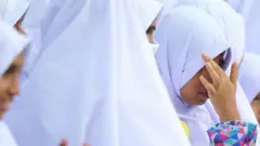 සුදු පැහැති මුස්ලිම් ආගමික ඇඳුම් වලින් සැරසී සිටින පාසල් දැරියක් පිරිසක්