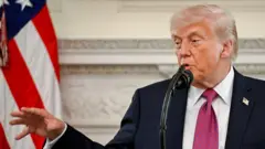 Donald Trump habla a un micrófono gesticulando y moviendo una mano. 