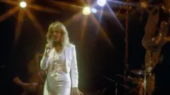 Bonnie Tyler está cantando con un vestido blanco en el escenario.