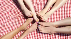 Vários pés femininos com as unhas pintadas em uma toalha de piquenique
