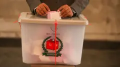 একটি ভোট বাক্সে সংসদ নির্বাচন ও গণভোটের সাদা ও গোলাপি দুই রংয়ের ব্যালট রাখছেন একজন, বাক্সের ভেতরে আরো কিছু ভোট দেখা যাচ্ছে। সম্প্রতি নির্বাচন কমিশন আয়োজিত মক ভোটের দিনের ছবি
