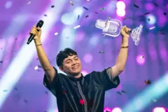 Muškarac sa podignutim rukama u vazduh nasmejan, u crnoj majici na sceni