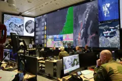 Pessoas trabalhando em sala repleta de computadores e telões onde informações de inteligência são monitoradas