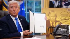 特朗普在橢圓形辦公室向記者發表演說時，手舉著一份有他簽名的行政命令。