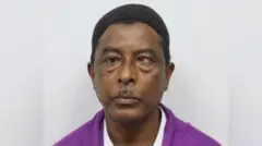 
頭に小さな黒いキャップをかぶり紫色のシャツを着た男性が、まっすぐ前を見つめている