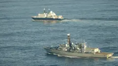 Yantar gemisi ve İngiliz donanmasına ait bir savaş gemisi görülüyor.