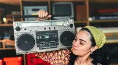 صورة لشابة تبدو سعيدة وهي تحمل على كتفها جهاز مسجل الكاسيت