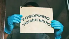 Чоловік тримає табличку "Говоримо українською"