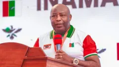 Perezida w'u Burundi Évariste Ndayishimiye arimo kuvugira mu ndangururamajwi. Yambaye isaha y'urushinge, impeta n'umupira w'amaboko magufi w'amabara y'umweru, umutuku n'icyatsi kibisi aranga ishyaka rya CNDD-FDD.