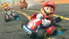 Cartoon of Mario in a red hat driving a cart from Mario Kart World. Princess Peach is driving a motorbike in the background.