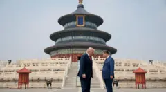 Los presidentes Trump y Xi permanecen de pie, uno frente al otro y con la cabeza ligeramente inclinada, ante unos escalones ornamentados que conducen a un grandioso templo chino de tres niveles, en tonos azules, verdes, rojos y dorados.
