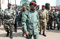 Image montrant le capitaine Moussa Dadis Camara, chef militaire de la Guinée, arrivant sur la place des Martyrs à Conakry le 2 octobre 2009 lors des cérémonies commémorant le 51e anniversaire de l'indépendance. Derrière lui, debout à sa droite Claude Pivi et Aboubacar Sidiki “Toumba” Diakité. 