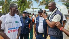 Uwari umurwayi mu mwambaro wera , abakozi ba OMS ku rundi ruhande, bose bishimira gutsina Ebola