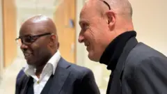 Charles Onana (i bubamfu) na Damien Sirieix bahagararanye, bamwenyura