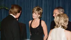 Diana, princesa de Gales, usa vestido preto sem mangas com detalhes brilhantes na parte superior, enquanto conversa com Donald Trump, que está de costas e veste um terno preto, em Nova York, em 1995