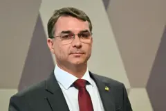 Flavio Bolsonaro é um homem branco. Ele usa óculos e está com um terno cinza e gravata vermelha.