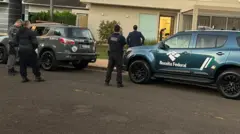 Carros da Polícia Militar e da Receita Federal estacionados em frente a casa de alto padrão alvo da Operação Fluxo Oculto. Também há agentes na calçada.