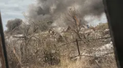 A shot through a window of a wasteland in Pokrovsk. The houses are severely damaged, the trees are bare and there is a large grey-black cloud in the distance