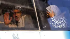 سيدة محجبة في باص تبكي، وأمامها شاب يلوح بيده أثناء توجههم لمعبر رفح